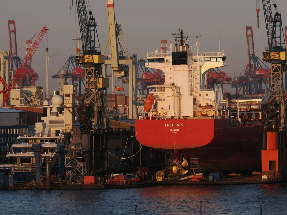 Ship in dry dock at a shipyard, with cranes behind